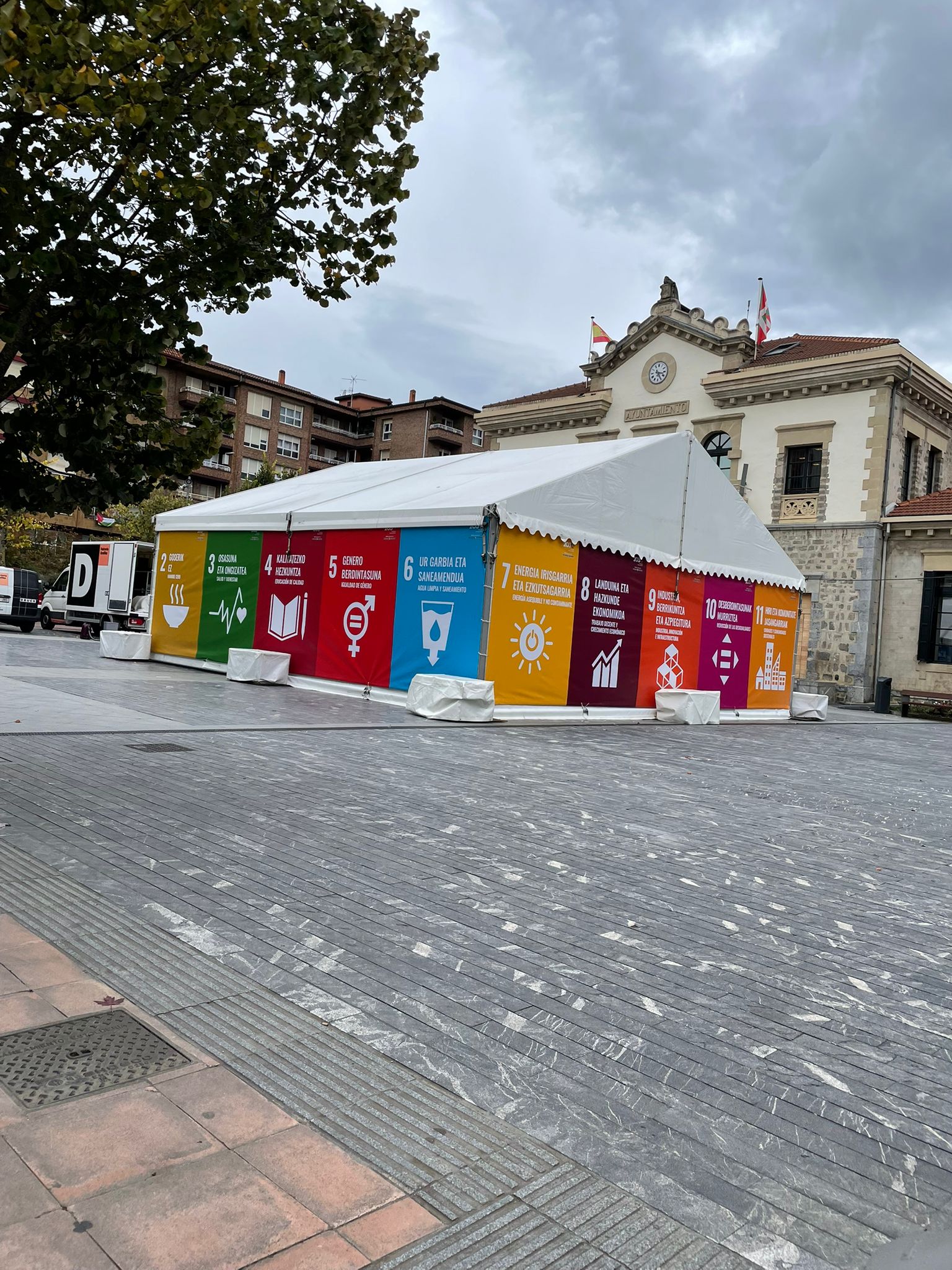 Carpa con gráficos coloridos de los ODS en un espacio público, junto a un edificio.