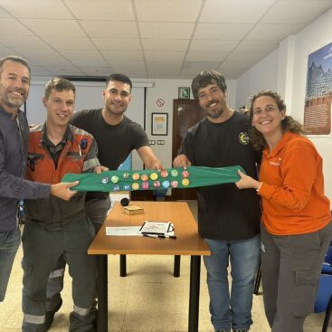Cuatro personas sosteniendo una tela verde con botones coloridos en una sala de reuniones.