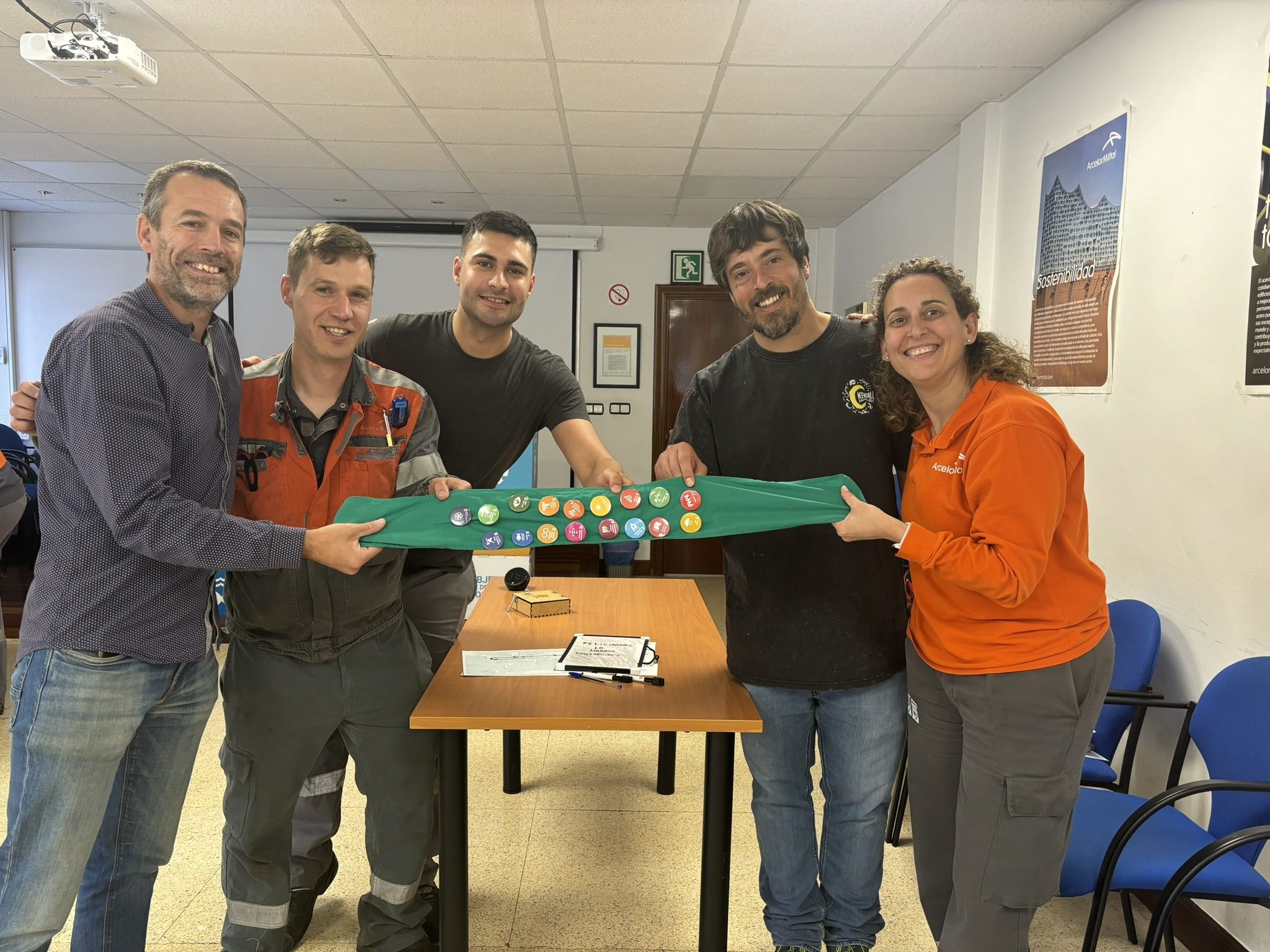 Cuatro personas sosteniendo una tela verde con botones coloridos en una sala de reuniones.