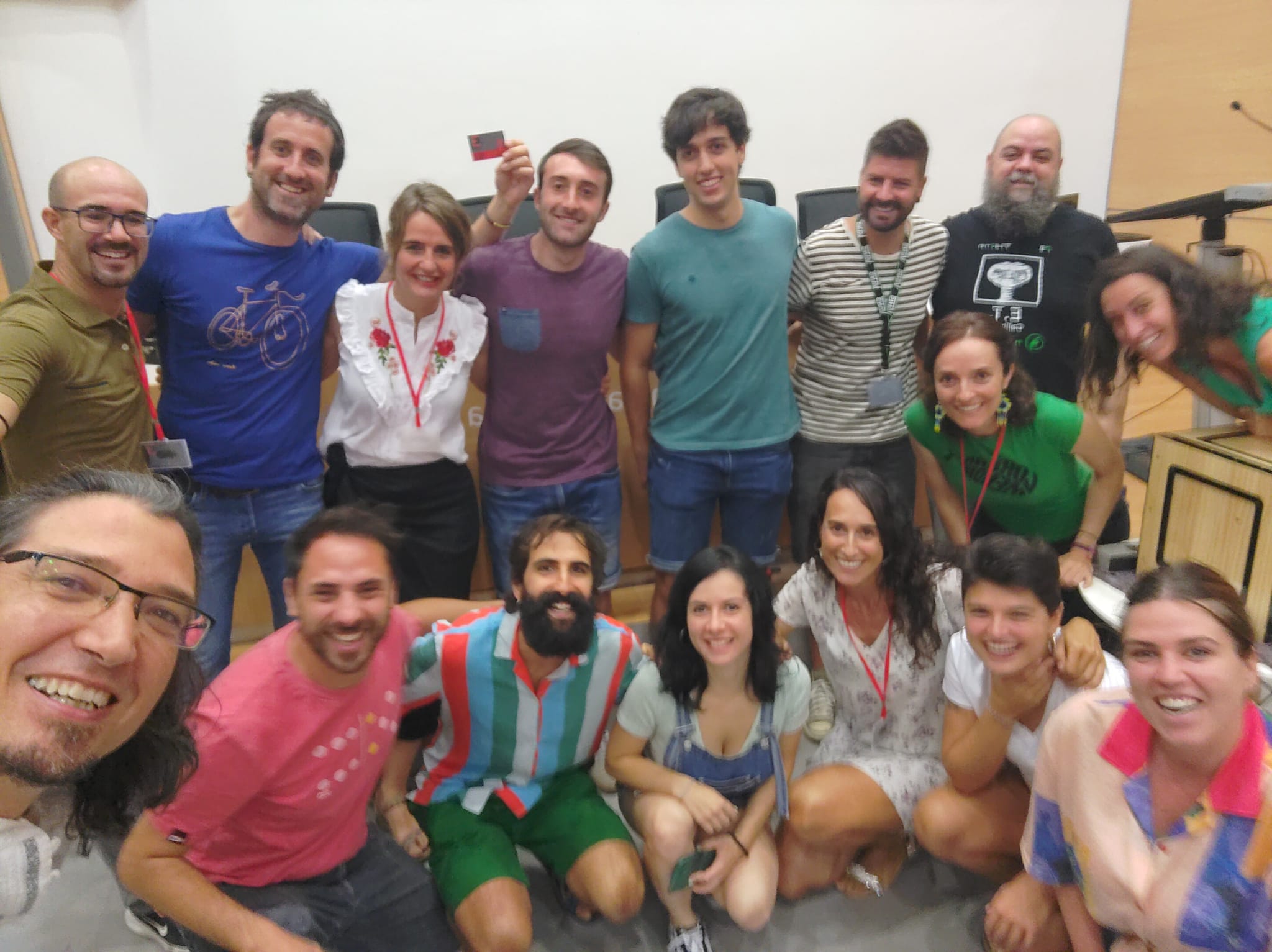 Grupo de personas sonriendo y posando en un evento, con algunos sosteniendo tarjetas.