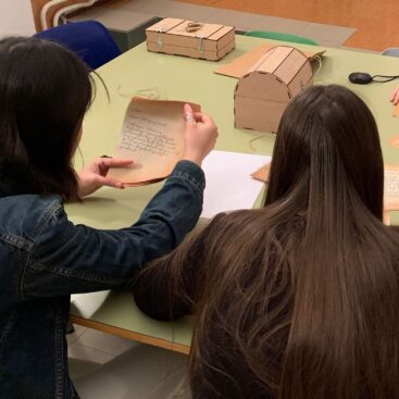 Dos personas sentadas en una mesa, revisando notas y cajas de madera.