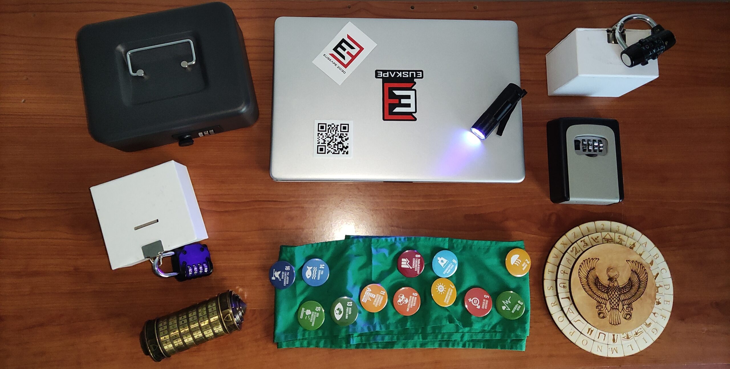 Varios objetos sobre una mesa, incluyendo una laptop, candados, un proyector y monedas.
